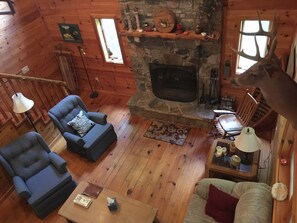 L’intérieur d’une cabane en rondins, avec une cheminée en pierre, deux fauteuils, un canapé et une table à manger.