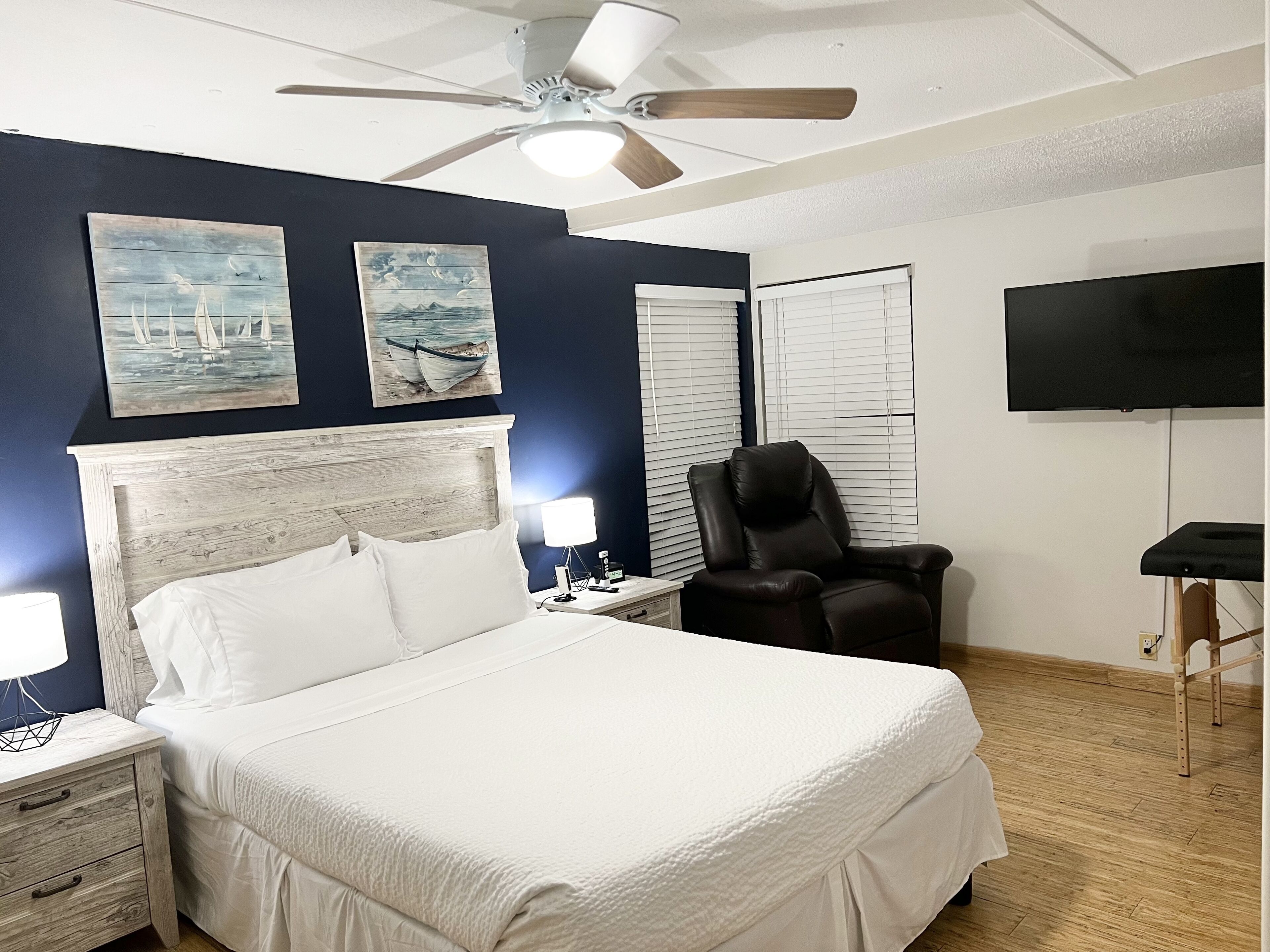 Une chambre à coucher comprenant un lit, des tables de chevet, une chaise, un ventilateur de plafond et des œuvres d’art accrochées au mur.