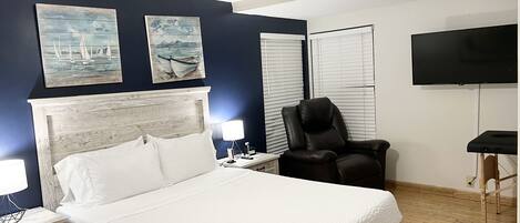 Une chambre à coucher comprenant un lit, des tables de chevet, une chaise, un ventilateur de plafond et des œuvres d’art accrochées au mur.