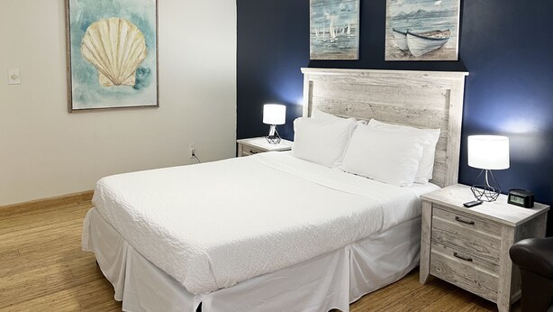 Een keurig opgemaakt slaapkamer met een bed, twee nachtkastjes met lampen, een plafondventilator en kunstwerken aan de muur.