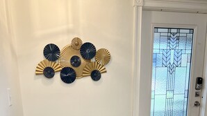Een eetgedeelte met een ronde tafel, twee grijze fauteuils met gouden poten, en decoratieve wandkunst erboven.