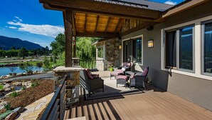 Eine überdachte Terrasse im Freien mit Korbmöbeln, Steinwänden und Blick auf einen See und Berge.