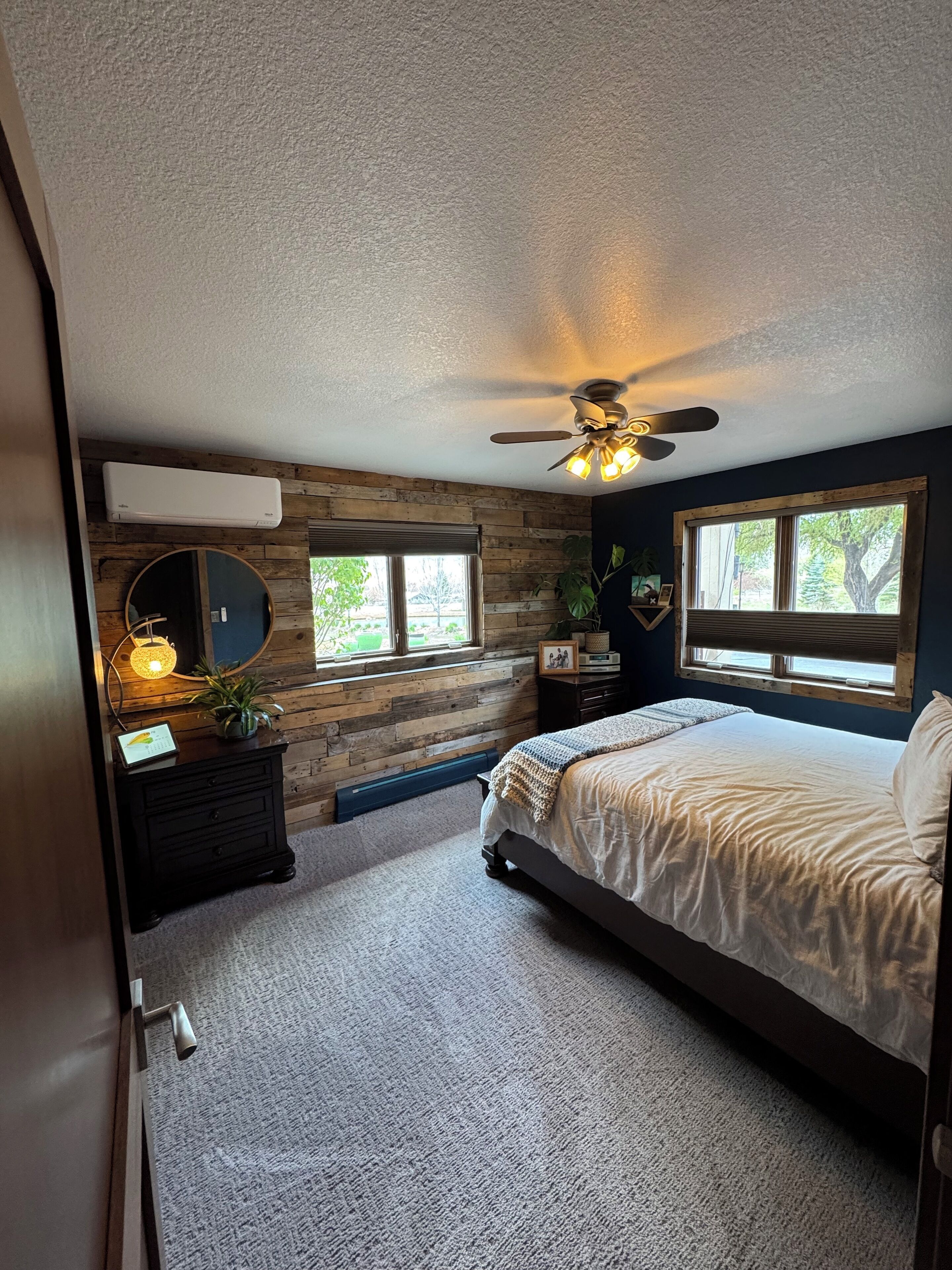 Een slaapkamer met een bed, een plafondventilator, een raam, een dressoir en een spiegel.