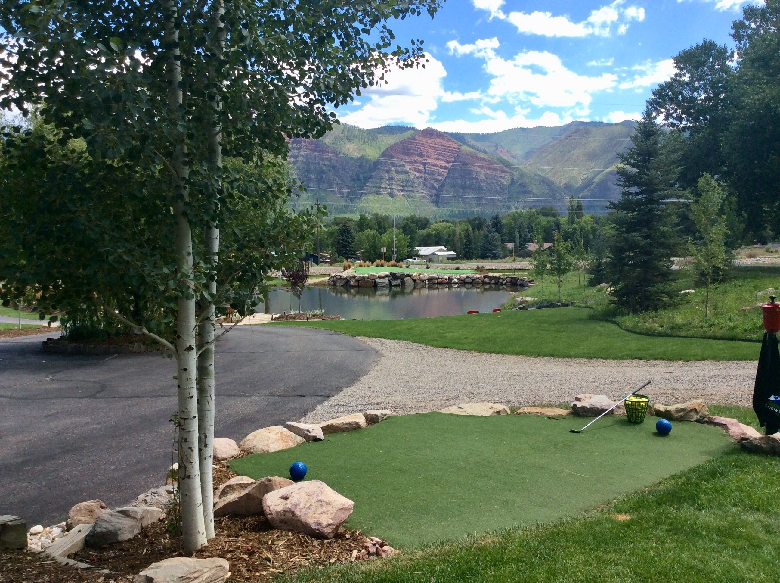 A golf course with a pond, trees, and mountains in the background.