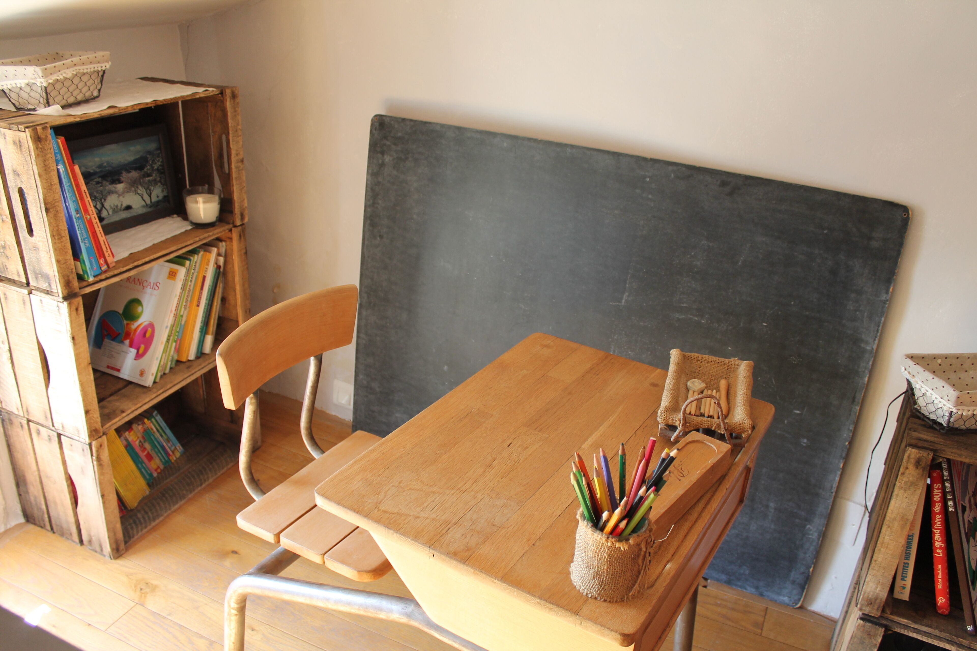 A classroom with a wooden desk, a chair, a blackboard, and a bookshelf filled with books.