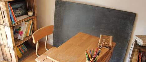 A classroom with a wooden desk, a chair, a blackboard, and a bookshelf filled with books.