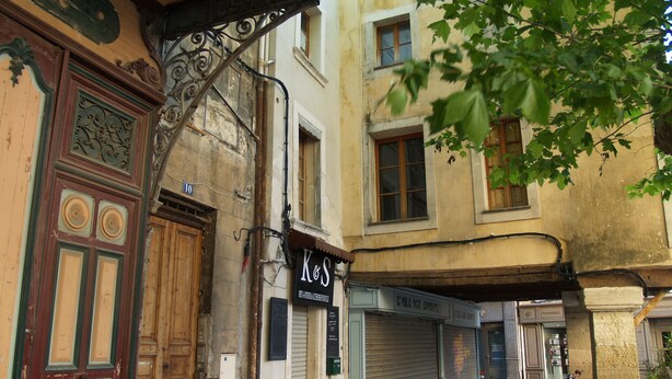 A narrow street with old buildings, a closed shop with a sign reading "K&S," and a motorcycle parked on the right.