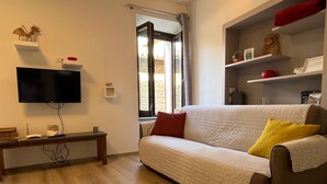 Un salon comprenant un canapé, un téléviseur à écran plat, une table basse en bois et une fenêtre avec des rideaux.