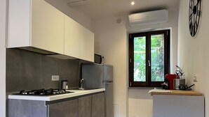 Une cuisine moderne dotée d’un îlot central, d’appareils électroménagers en acier inoxydable et d’une fenêtre donnant sur un espace verdoyant.