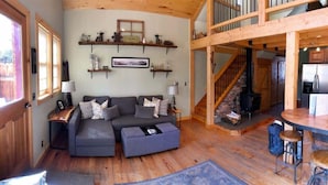 Uma sala de estar aconchegante com sofá seccional, piso de madeira, lareira e área de cozinha com mesa de jantar e banquetas.