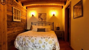 Um quarto estilo cabana de madeira, com uma cama, duas luminárias fixadas na parede, uma mesa de cabeceira e um quadro emoldurado na parede.