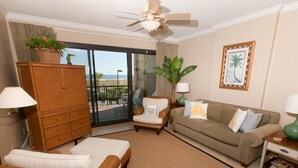A living room with a wicker sofa, a brown couch, a wicker ottoman, a wooden cabinet, and a view of the beach through a sliding glass door. - GRAND POINTE 211....LOVELY CONDO, BEST VIEW, CLOSE TO AMENITIES  (Orange Beach)