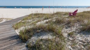 A beach with a wooden boardwalk leading to a sandy area with a red chair. - GRAND POINTE 211....LOVELY CONDO, BEST VIEW, CLOSE TO AMENITIES  (Orange Beach)