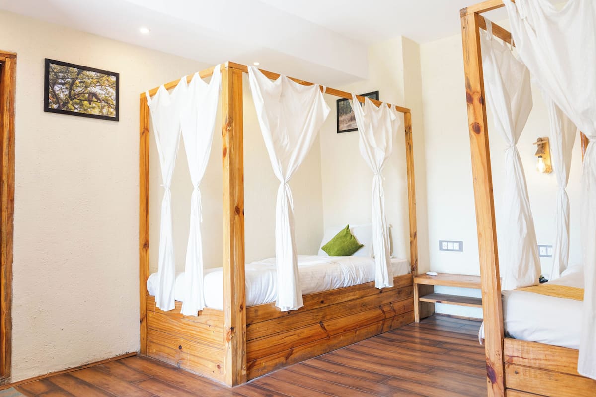 Quarto com cama de dossel de madeira, um banco e luminária fixada na parede.