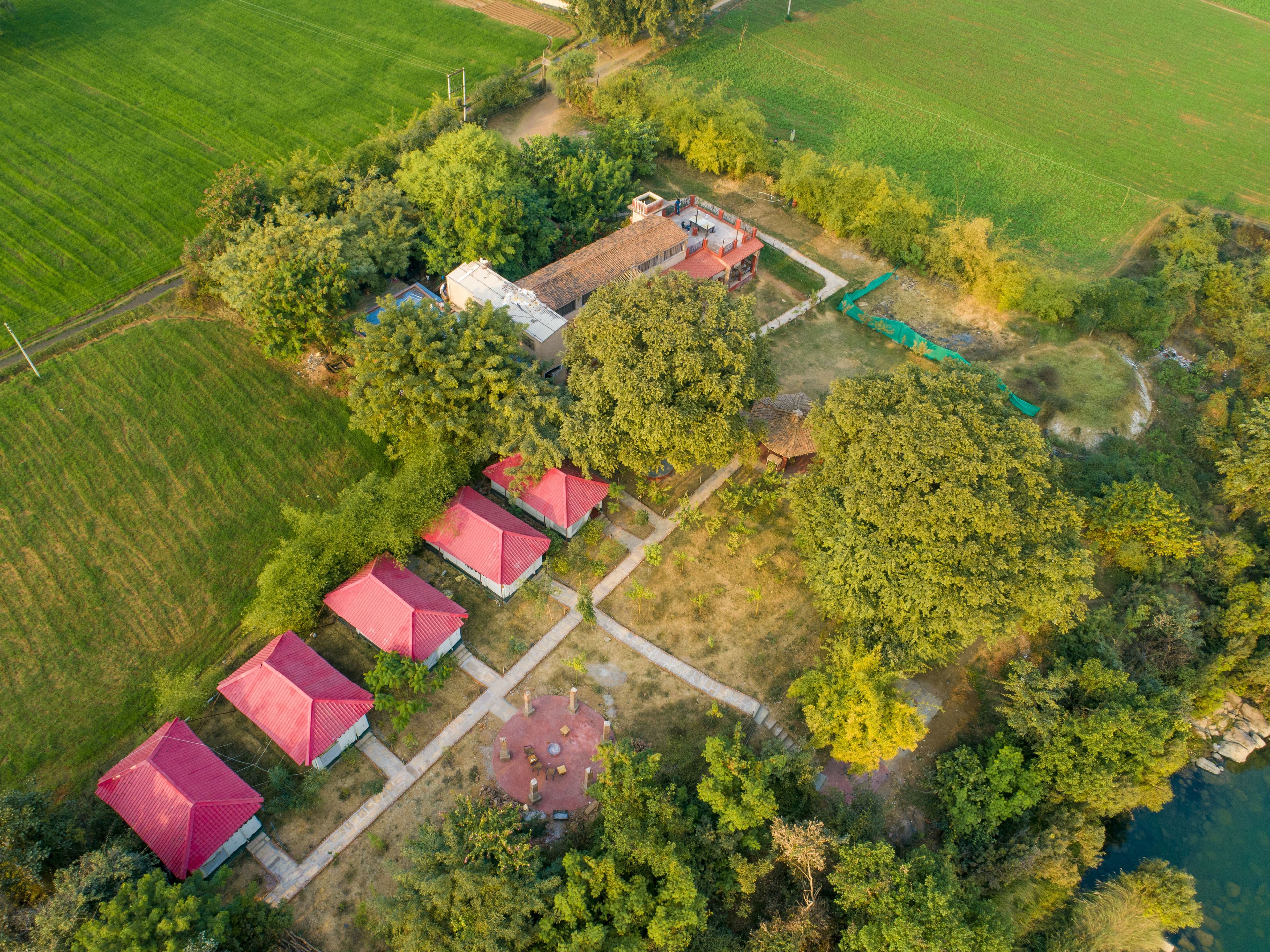 Vista aérea de una propiedad con varios edificios de techo rojo, un área central abierta con asientos y campos verdes y árboles circundantes.