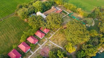 Vista aérea de una propiedad con varios edificios de techo rojo, un área central abierta con asientos y campos verdes y árboles circundantes.