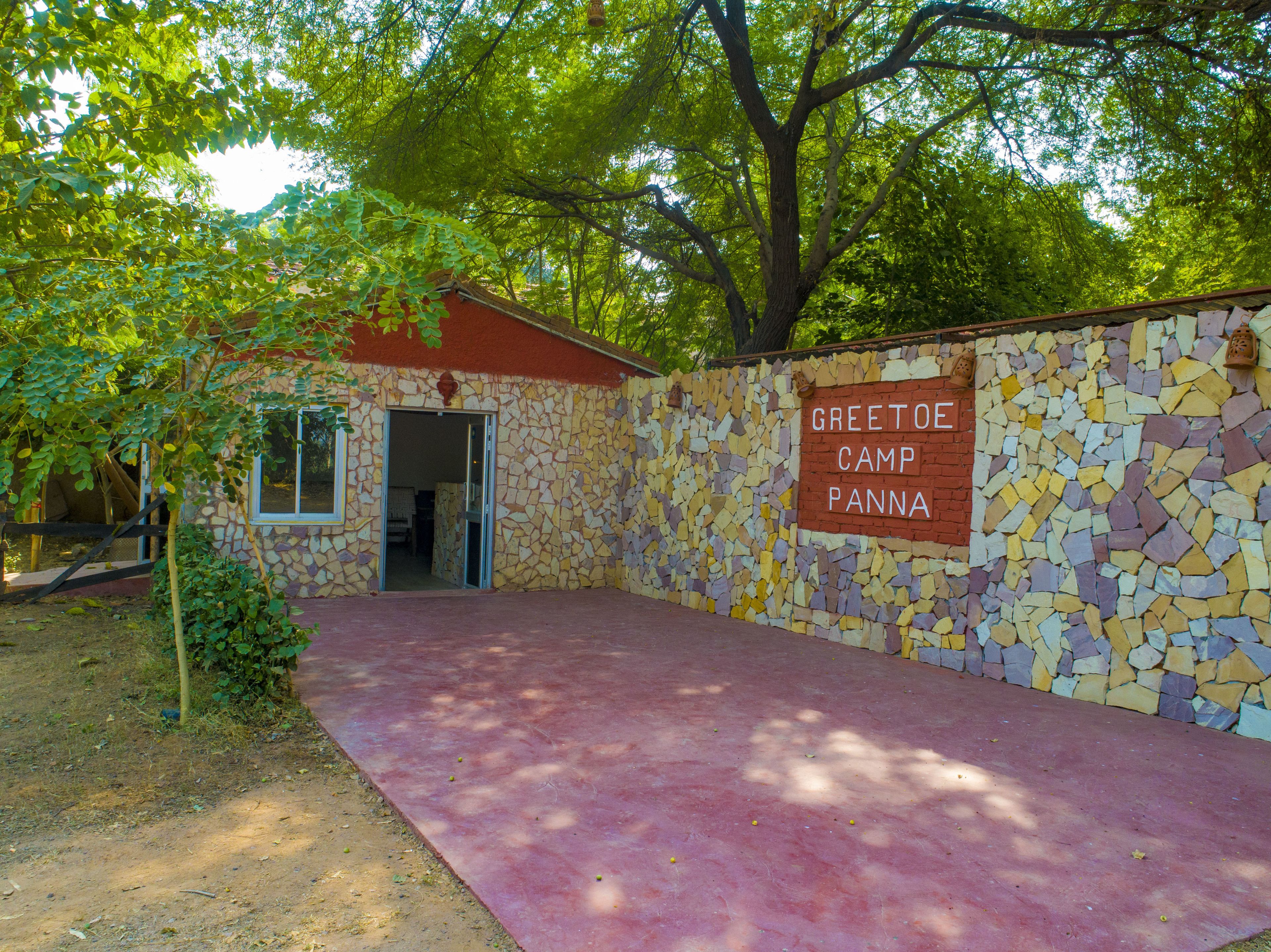 A stone building with a mosaic wall and a red roof, labeled "Greetoo Camp Panna."