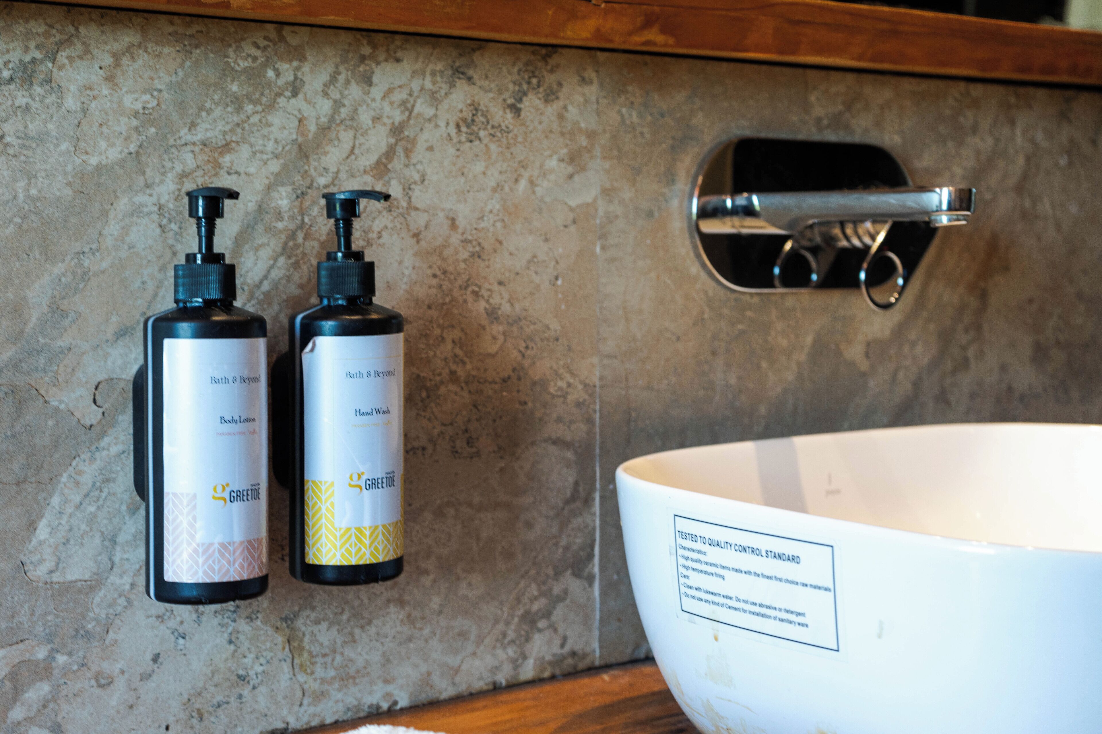 A bathroom with a white sink and two bottles of lotion labeled 'GREETIE' on a textured wall.