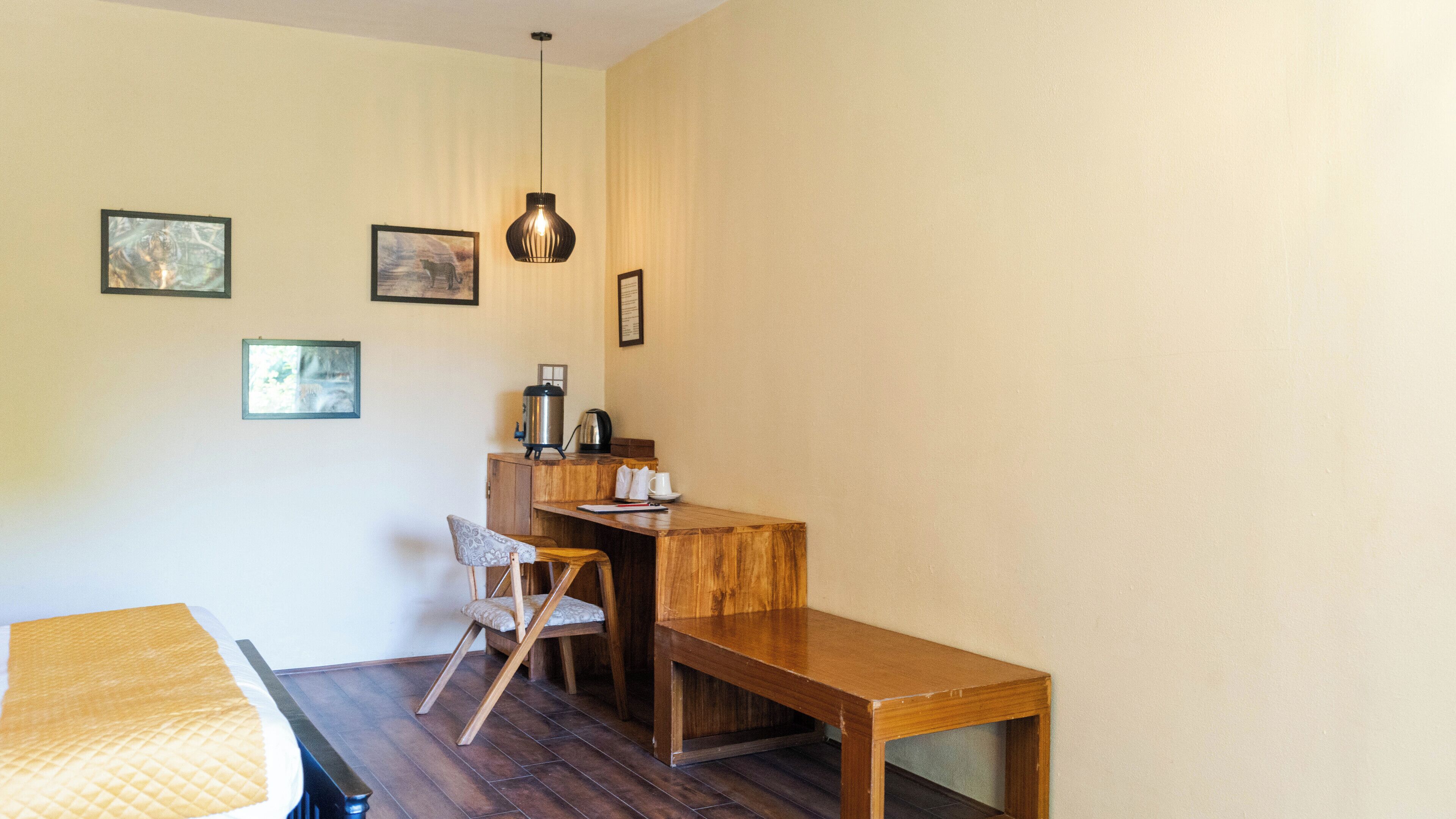 A small, cozy room with a wooden desk, a chair, and a bench. There are framed pictures on the wall and a hanging light fixture.