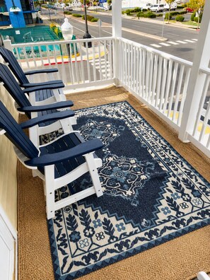 A covered porch with a patterned rug, white railing, and blue chairs.