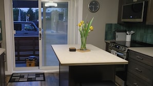 Una cocina con una isla central, microondas y estufa. Hay una puerta corrediza de vidrio que da a un garaje con un coche aparcado.