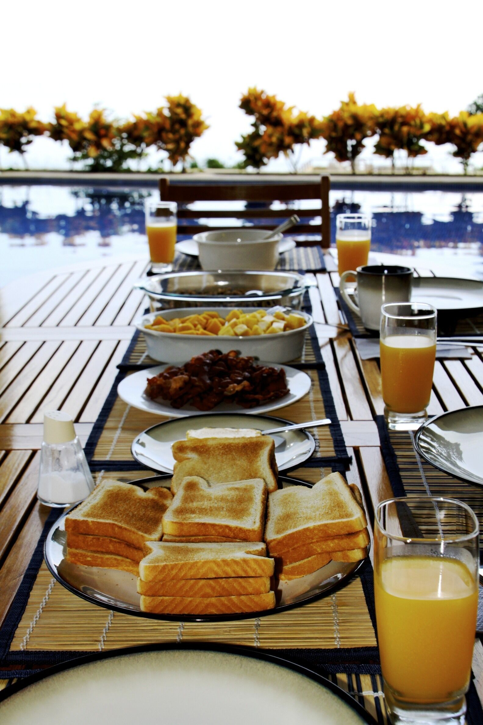 A breakfast table with toast, fruit, and juice, overlooking a pool.