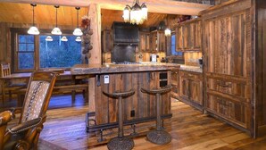 Cocina rústica con muebles de madera, una isla central con taburetes e iluminación colgante.