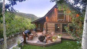 Una cabaña de troncos con terraza, mobiliario exterior y una chimenea.