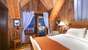 Un dormitorio de cabaña de madera con una cama, una silla, una mesita y un televisor en la pared.