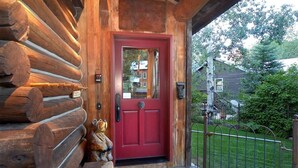 A log cabin with a red door, a wooden porch, and a metal gate.