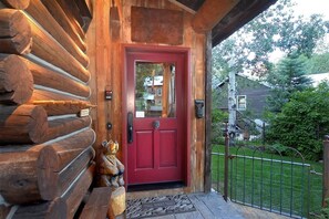 A log cabin with a red door, a wooden porch, and a metal gate.