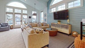 A spacious living room with a large sofa, a coffee table, and a TV mounted on the wall.