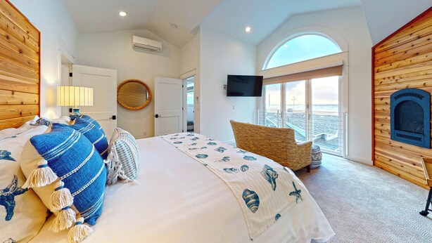 A bedroom with a large bed, a television, a fireplace, and a view of the ocean.