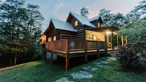 Eine Holzblockhütte mit einer Holzdiele und einem Metalldach, umgeben von Bäumen.