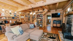 Ein gemütliches Blockhaus-Interieur mit Holzbalkendecke, einer Couch, einem Kamin und einem Fernseher.
