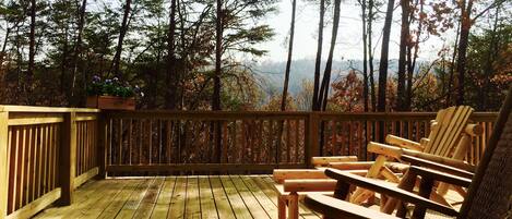 A wooden deck with chairs and a table, surrounded by tall trees and a view of the mountains.