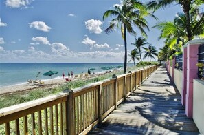 A wooden boardwalk leading to a beach with palm trees and umbrellas.