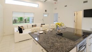 Una cocina moderna con una isla central, armarios blancos y una zona de comedor con un sofá blanco.