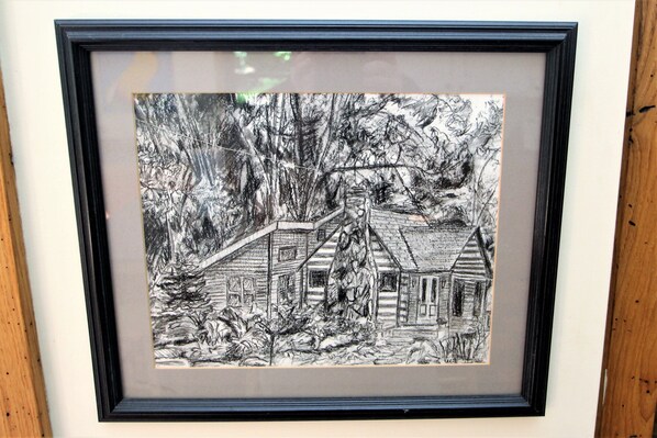 Dibujo en blanco y negro enmarco que muestra una cabaña rodeada de árboles.
