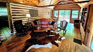 A log cabin interior with a leather sofa, chairs, a dining table, and a cowhide rug. - Fayette Springs--Creek House--Enjoy this Spacious Cottage! (Farmington)