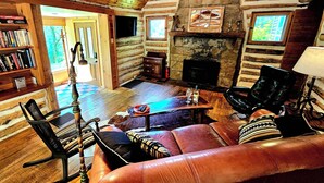 A log cabin interior with a fireplace, leather sofa, and a bookshelf. - Fayette Springs--Creek House--Enjoy this Spacious Cottage! (Farmington)