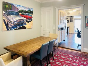 Un coin repas avec une table et des chaises en bois, un tapis à motifs rouges et un tableau représentant des voitures anciennes accroché au mur.