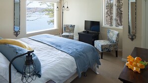 Une chambre avec un grand lit, deux fauteuils, une télévision et une vue sur un lac.