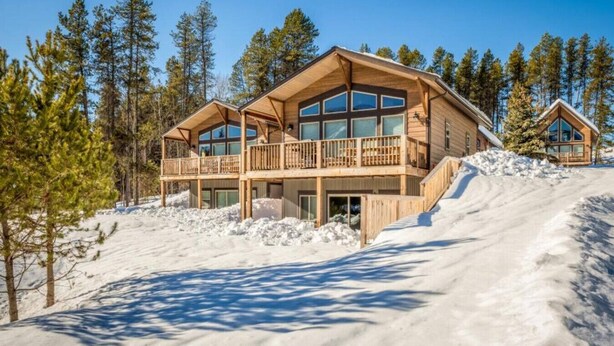 Een houten chalet met balkon, omgeven door sneeuw en bomen.