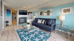 Una sala de estar con un sofá azul, chimenea, televisor de pantalla plana y estantería.