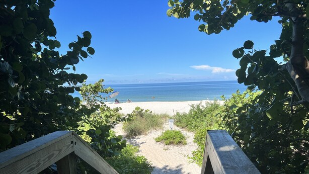 Een houten pad dat naar een strand leidt, met een helder uitzicht op de oceaan.