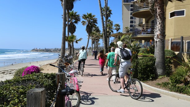 Une promenade en bord de mer bordée de palmiers, une plage et un immeuble doté de balcons.