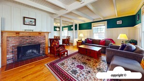 A spacious living room with a brick fireplace, wooden flooring, and a large window. - HOT TUB: ESCAPE MANOR: 600ft to BEACH:  Seaside Vacation Homes, Inc Managed  (Seaside)