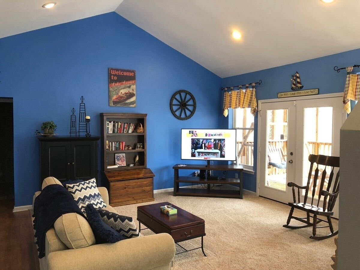 A living room with a blue wall, a television, a bookshelf, a coffee table, and a rocking chair.