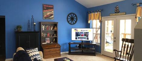 A living room with a blue wall, a television, a bookshelf, a coffee table, and a rocking chair.